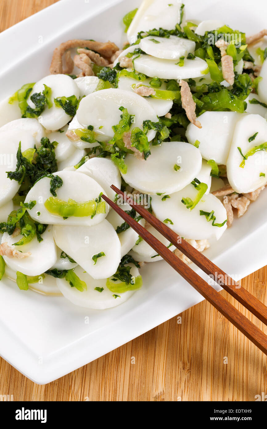 L'immagine verticale cinese di riso tagliatelle con fettine di maiale in bianco con piastra di bamboo naturale sullo sfondo Foto Stock
