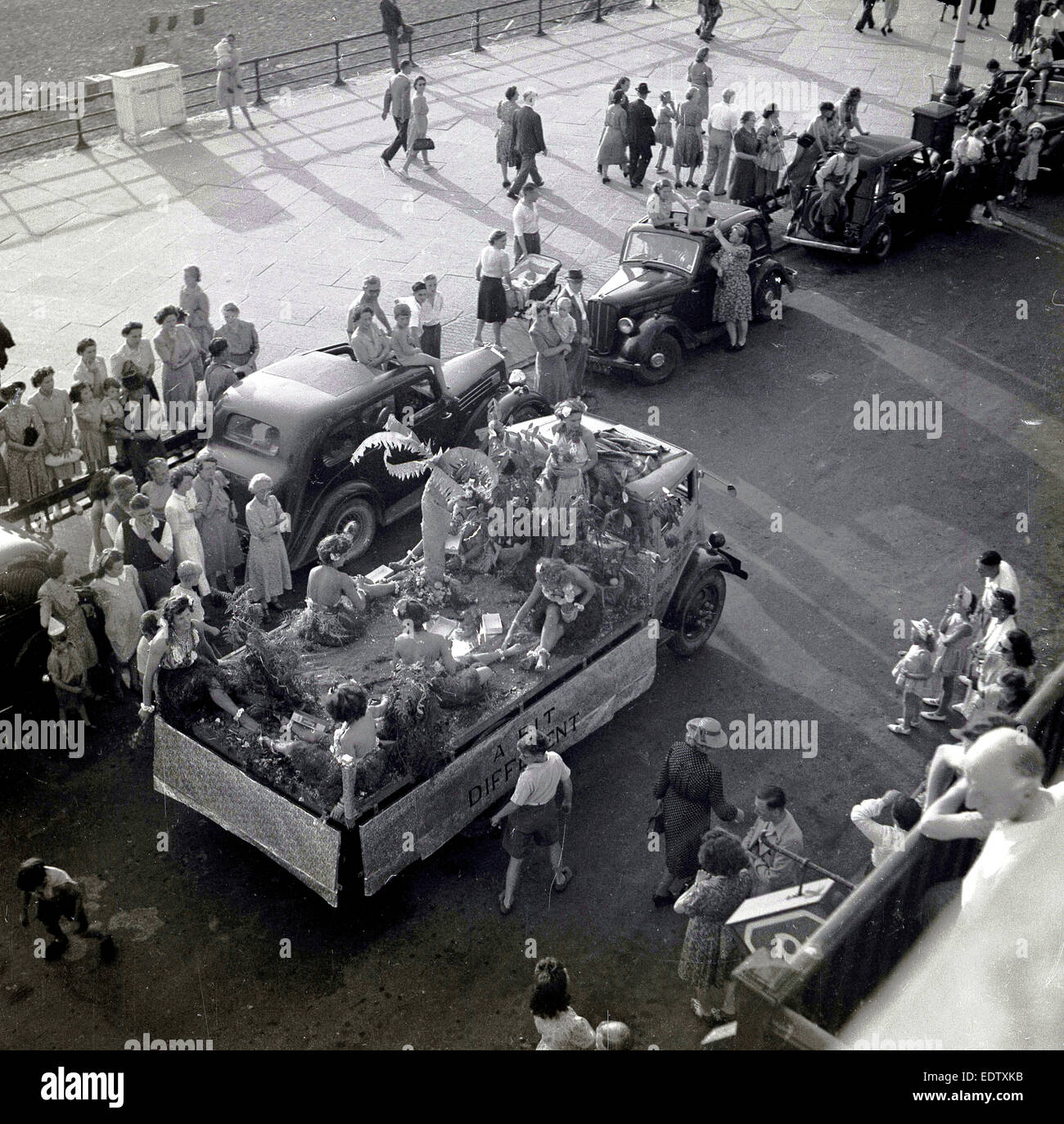 Anni Cinquanta foto storiche da sopra illustrante le ragazze vestite di tipo hawaiano gonne seduti nella parte posteriore di un carrello () di flottazione dal titolo 'un po' diverso nella strada di carnevale o 'Kiddies Karnival', lungo il lungomare a Aberystwyth, Wales, Regno Unito. Foto Stock