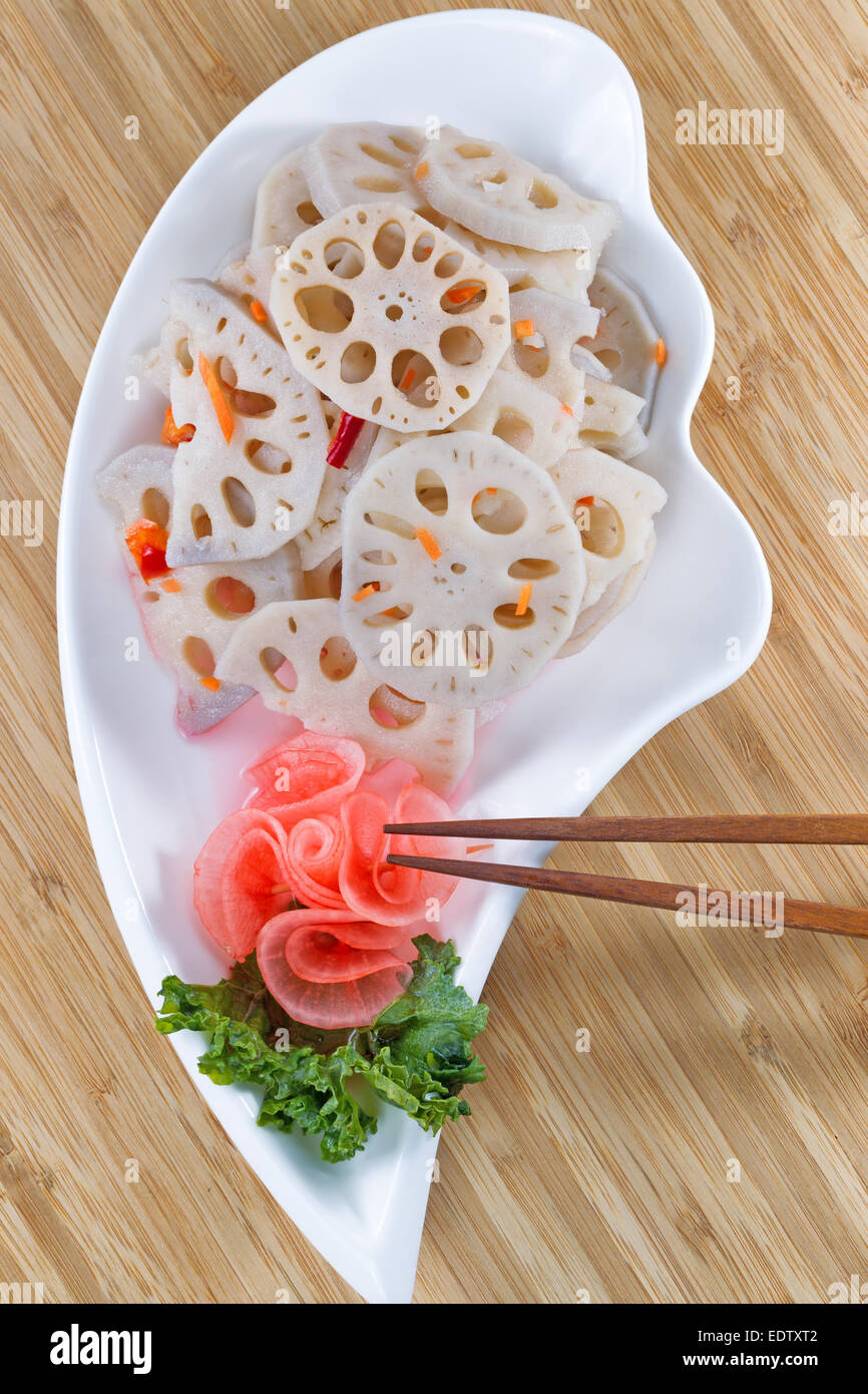 Vista dall'alto l'immagine verticale di cinesi lotus acqua ravanello nel piatto bianco, con bacchette in bamboo naturale sullo sfondo Foto Stock