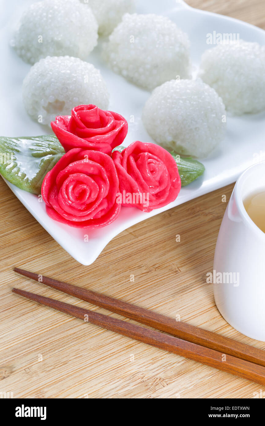 L'immagine verticale di dolci Cinesi di riso appiccicoso sfere, in background, rosso della decorazione rose, e il tè verde con bamboo naturale Foto Stock