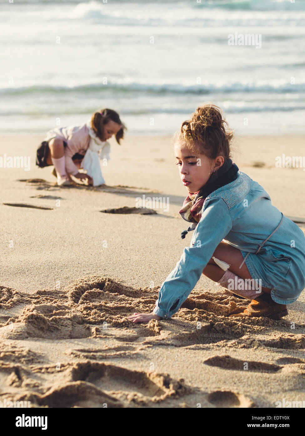 Due bambine squatting e giocando sulla spiaggia in un pomeriggio soleggiato Foto Stock