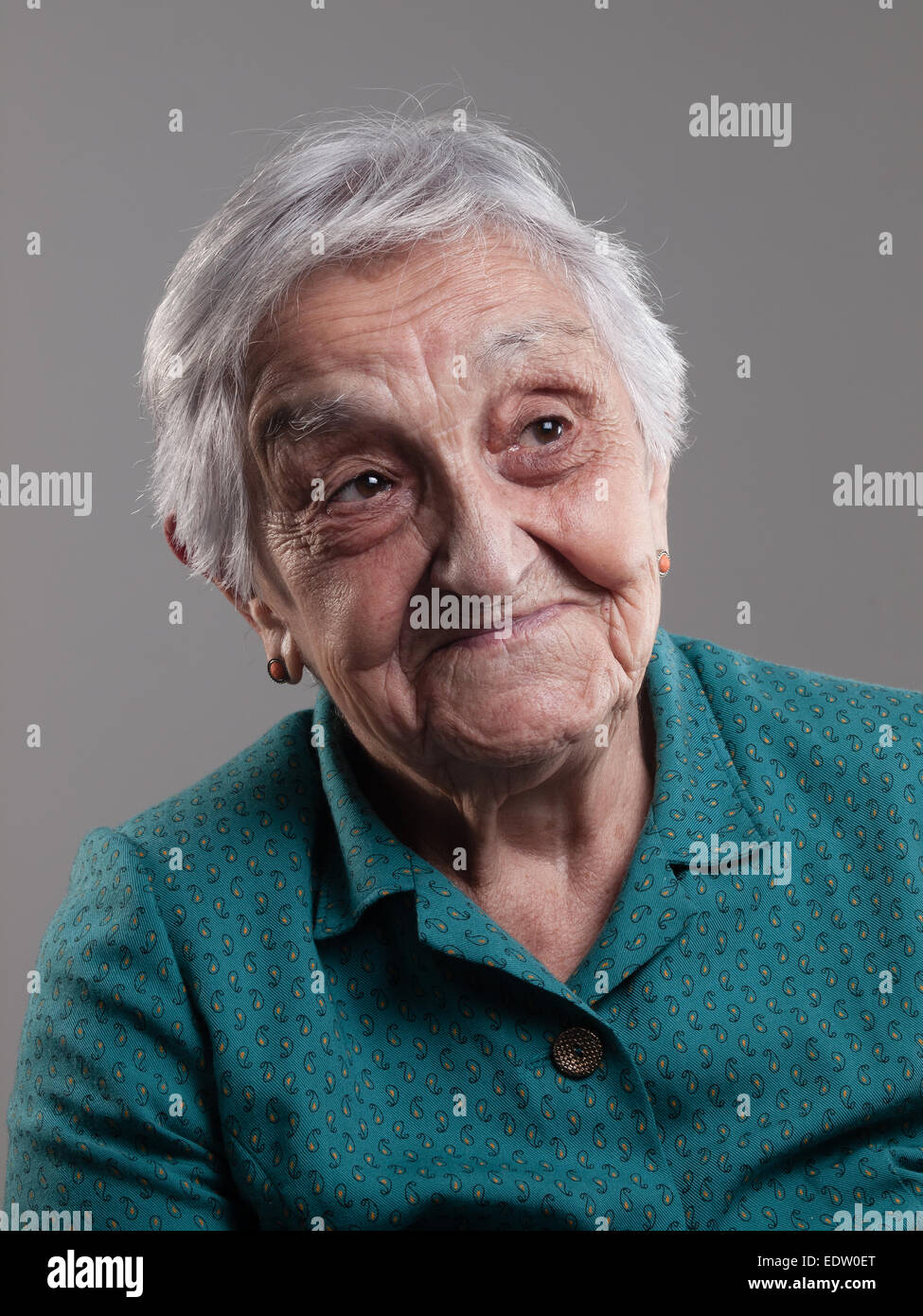 Donna anziana con espressione positiva in un studio shot e isolate su uno sfondo grigio Foto Stock