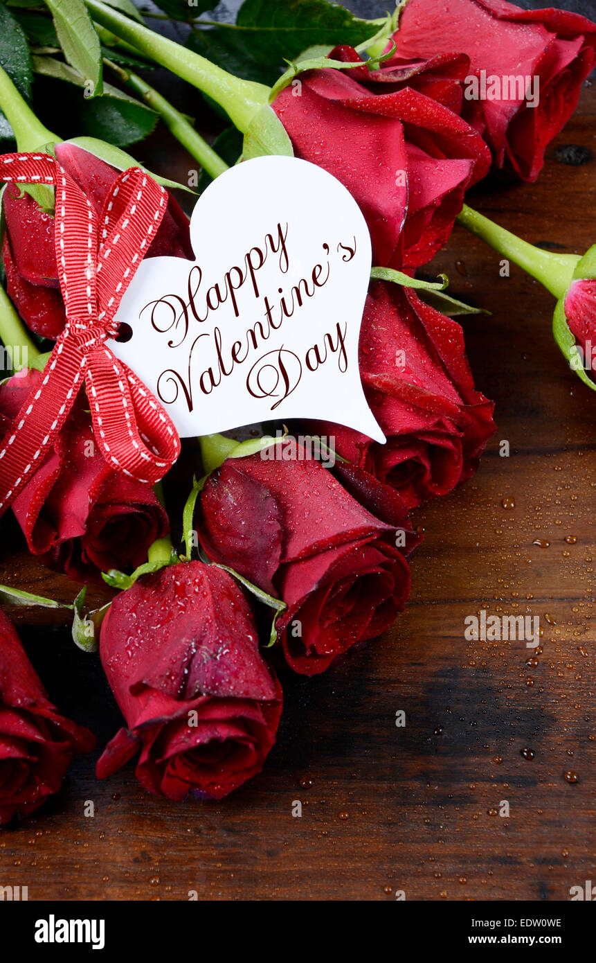 Buon San Valentino rose rosse su scuro legno riciclato lo sfondo con il saluto a forma di cuore dono tag - verticale. Foto Stock