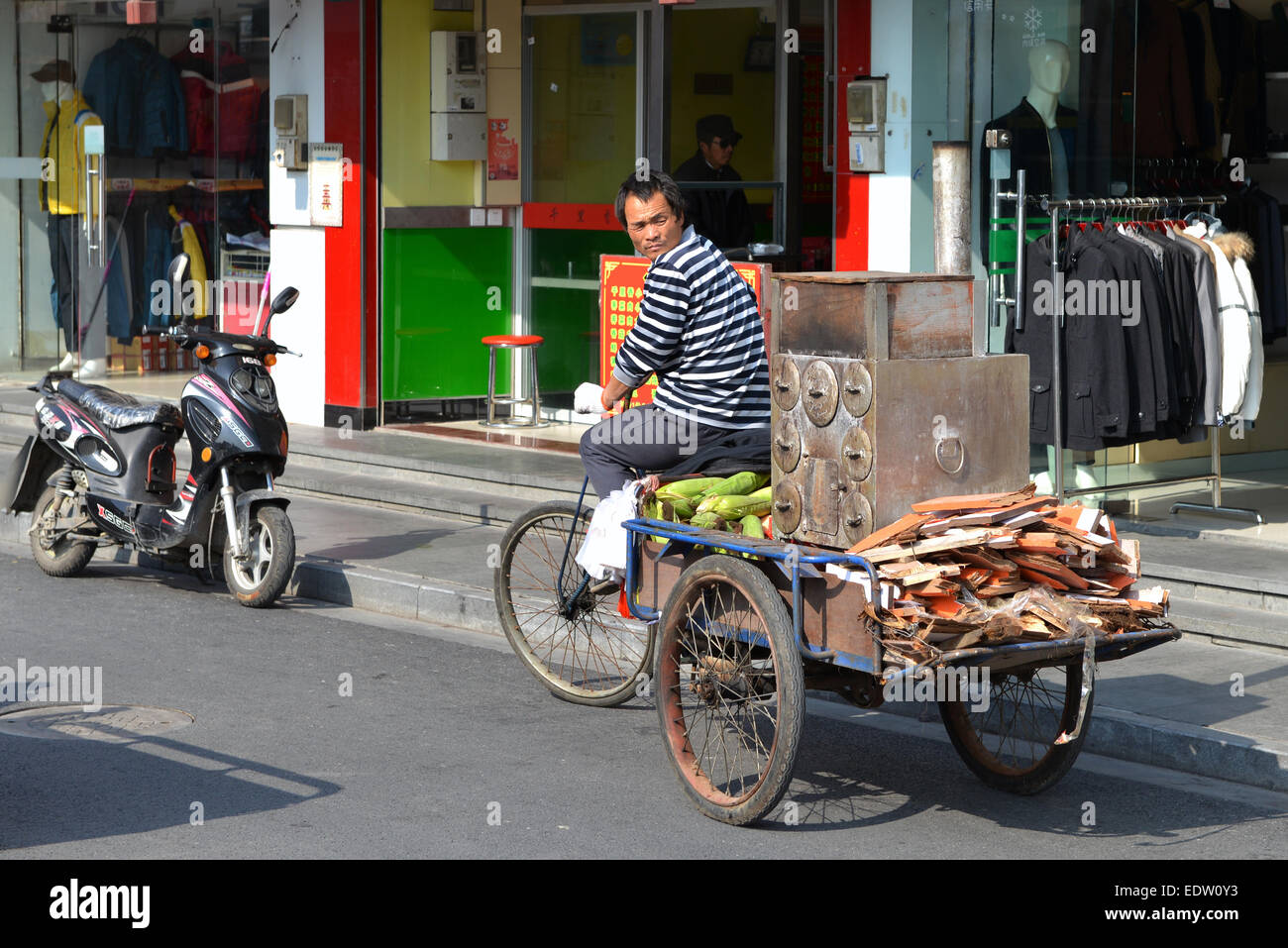 Un uomo che cavalca un portable tostatore che gli consente di vendere il mais tostato nel distretto Qingpu di Shanghai. Foto Stock