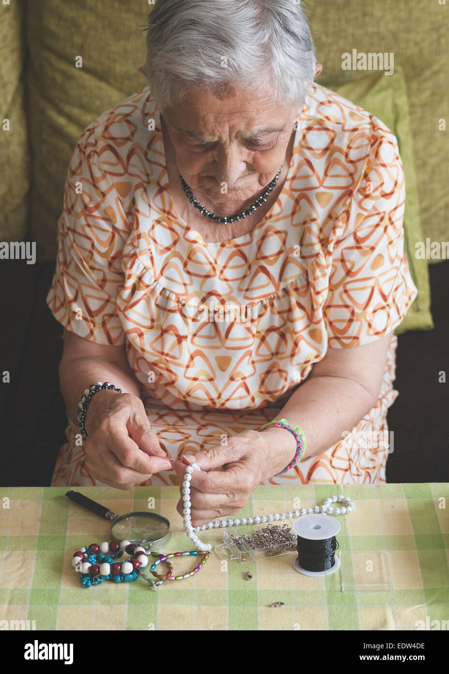 Donna anziana facendo una collana a casa Foto Stock