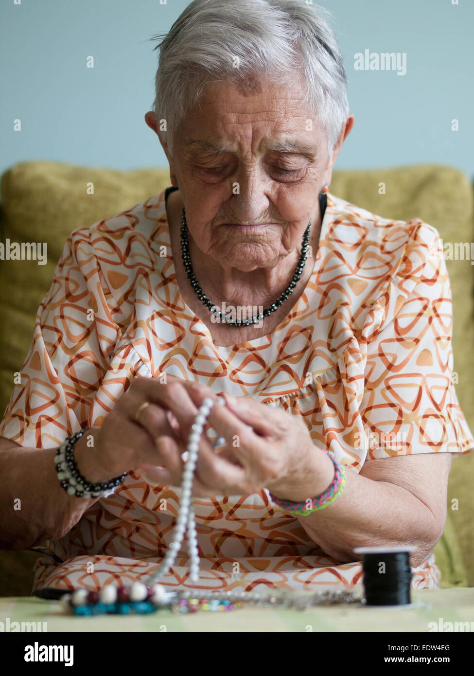 Donna anziana facendo collane in casa sua Foto Stock
