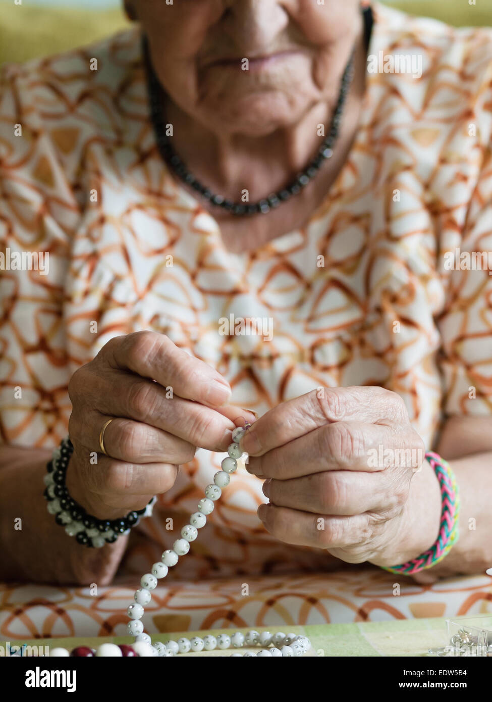 Donna anziana facendo collane in casa sua Foto Stock