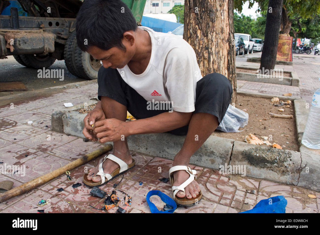 Un uomo che lavora come scavenger elimina piccole schede a circuito elettronico da piccolo apparecchio tappi in libertà Park a Phnom Penh, Foto Stock