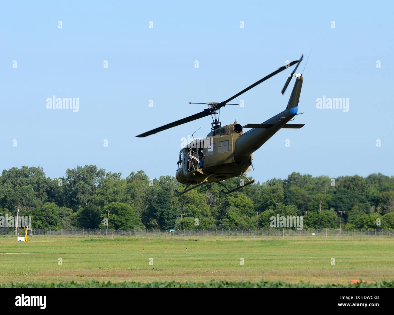 Il camuffamento verde elicottero militare UH-1 Huey volare al di sopra di un campo Foto Stock