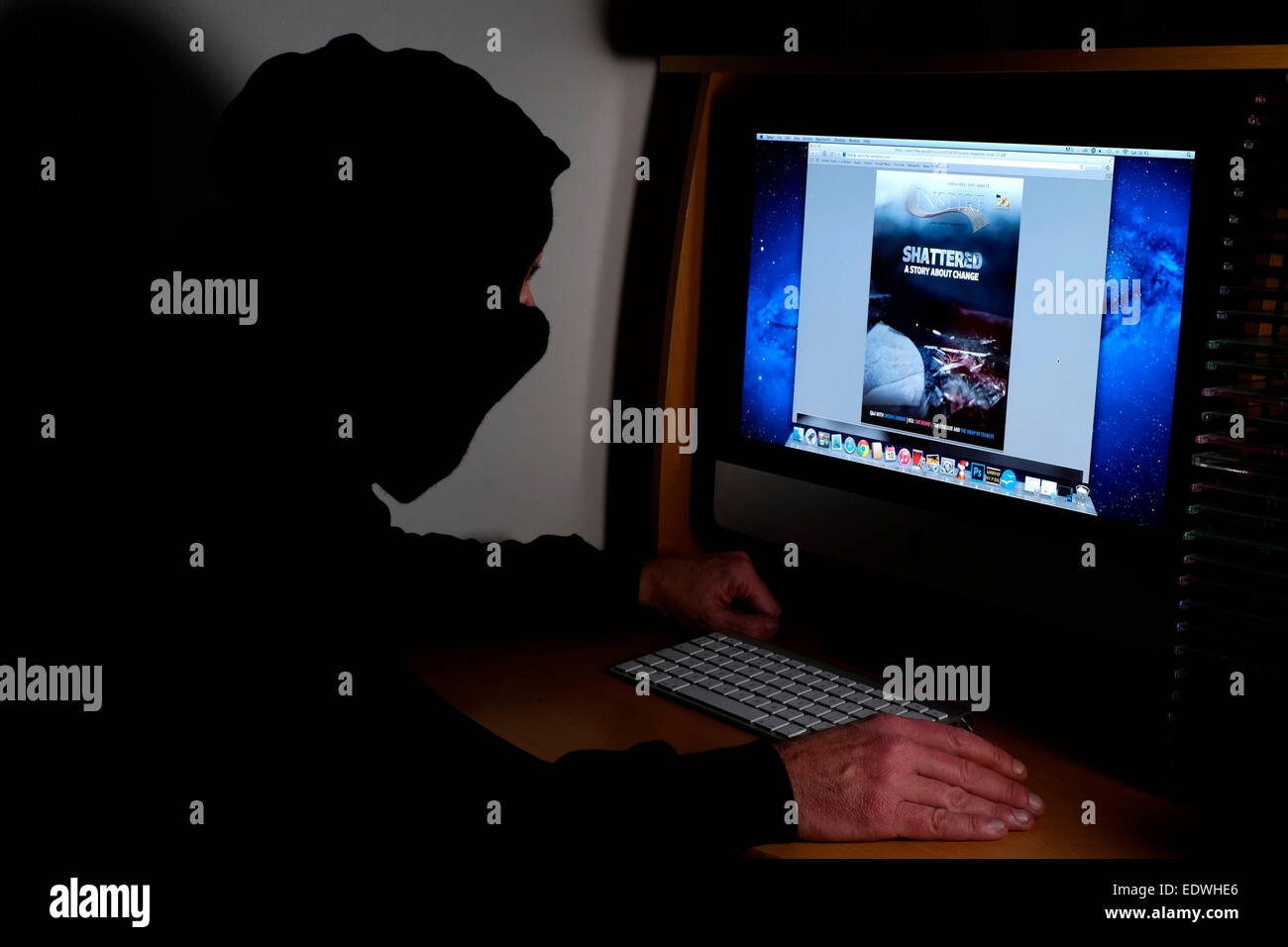 Incappucciato e uomo mascherato seduto al suo computer la lettura della versione on line di al Qaeda terroristici magazine ispirare Foto Stock