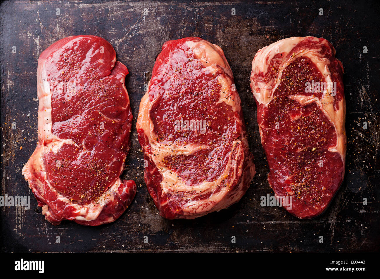 Tre tagli di materie fresche bistecche di carne e condimenti su sfondo scuro Foto Stock