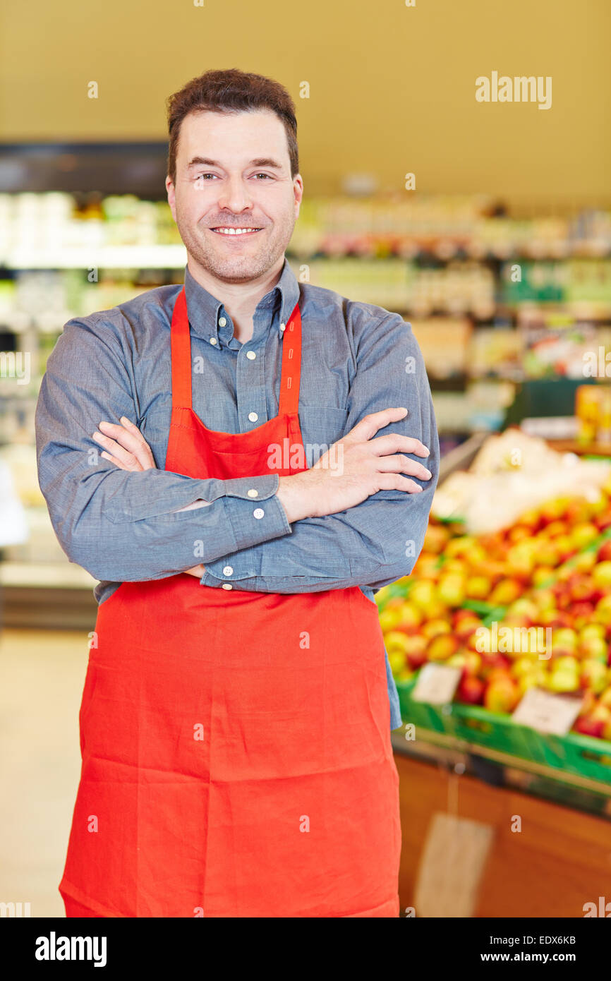Sorridente venditore in piedi con le braccia incrociate in un supermercato Foto Stock