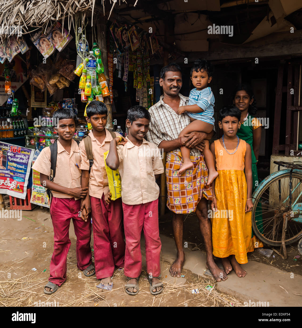 THANJAVUR, India - 13 febbraio: una scuola non identificato i bambini in uniforme e l'uomo con il bambino in piedi vicino al negozio di rurale. L'India, Foto Stock