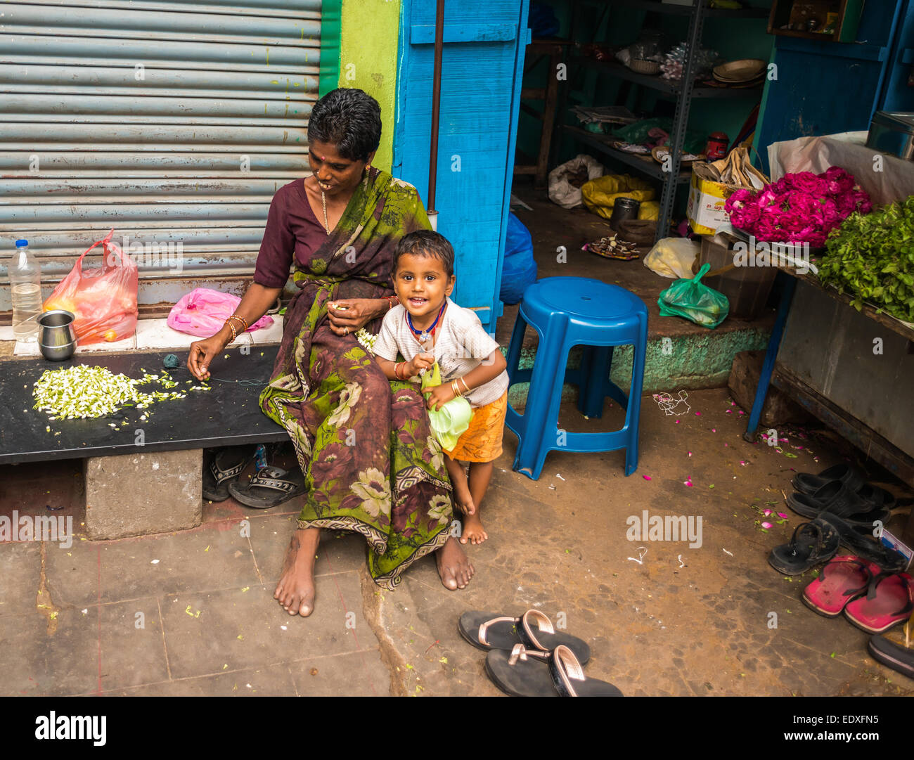 THANJAVOUR, India - 14 febbraio: un bambino non identificato e una donna nel tradizionale costume indiano sono seduti. La donna tesse una garl Foto Stock