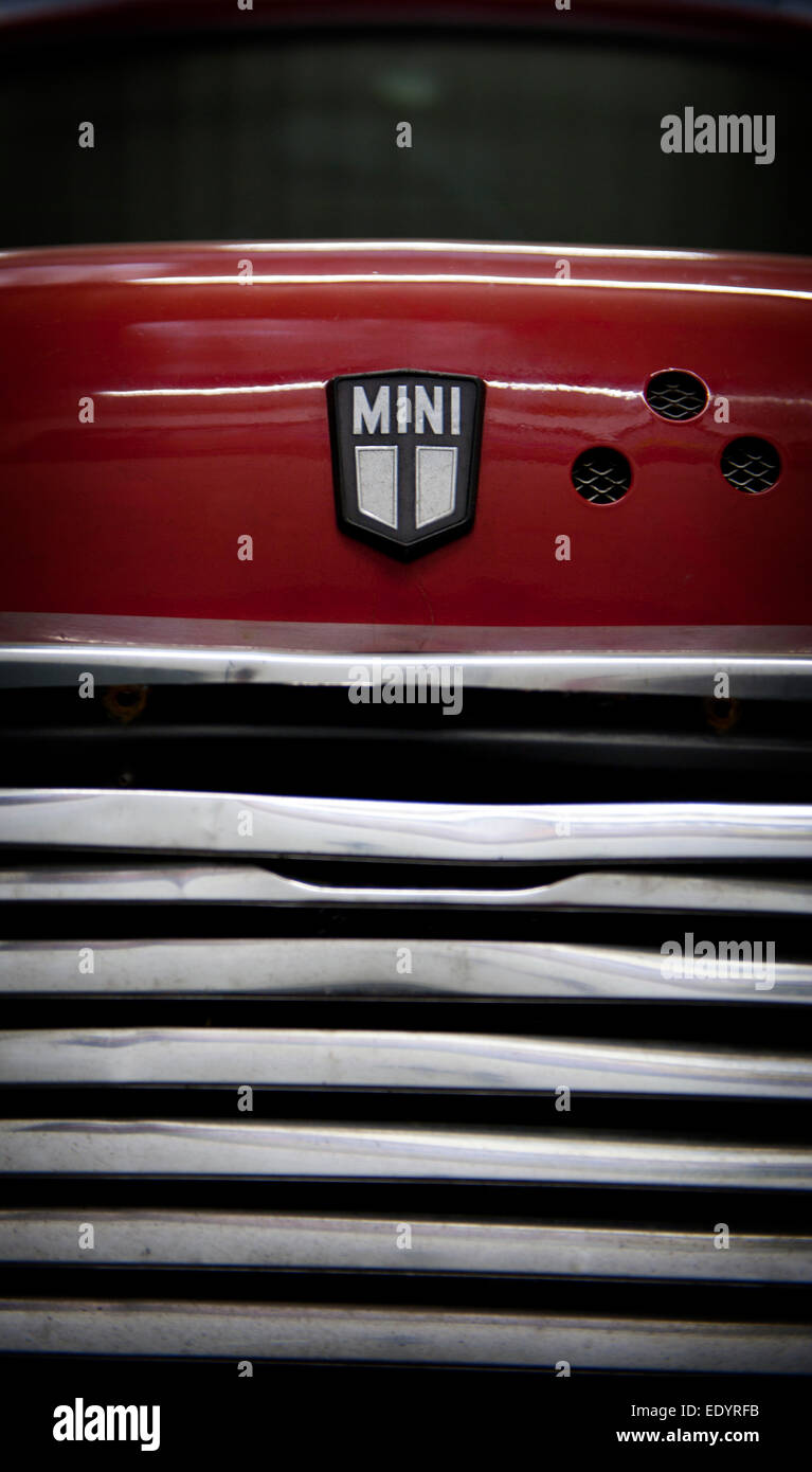 Primo piano, dettaglio macro di un logo rosso Mini Cooper sul cofano e spranghe nere della griglia, che mostra l'emblema iconico del marchio e l'audace contrasto di colore. Foto Stock