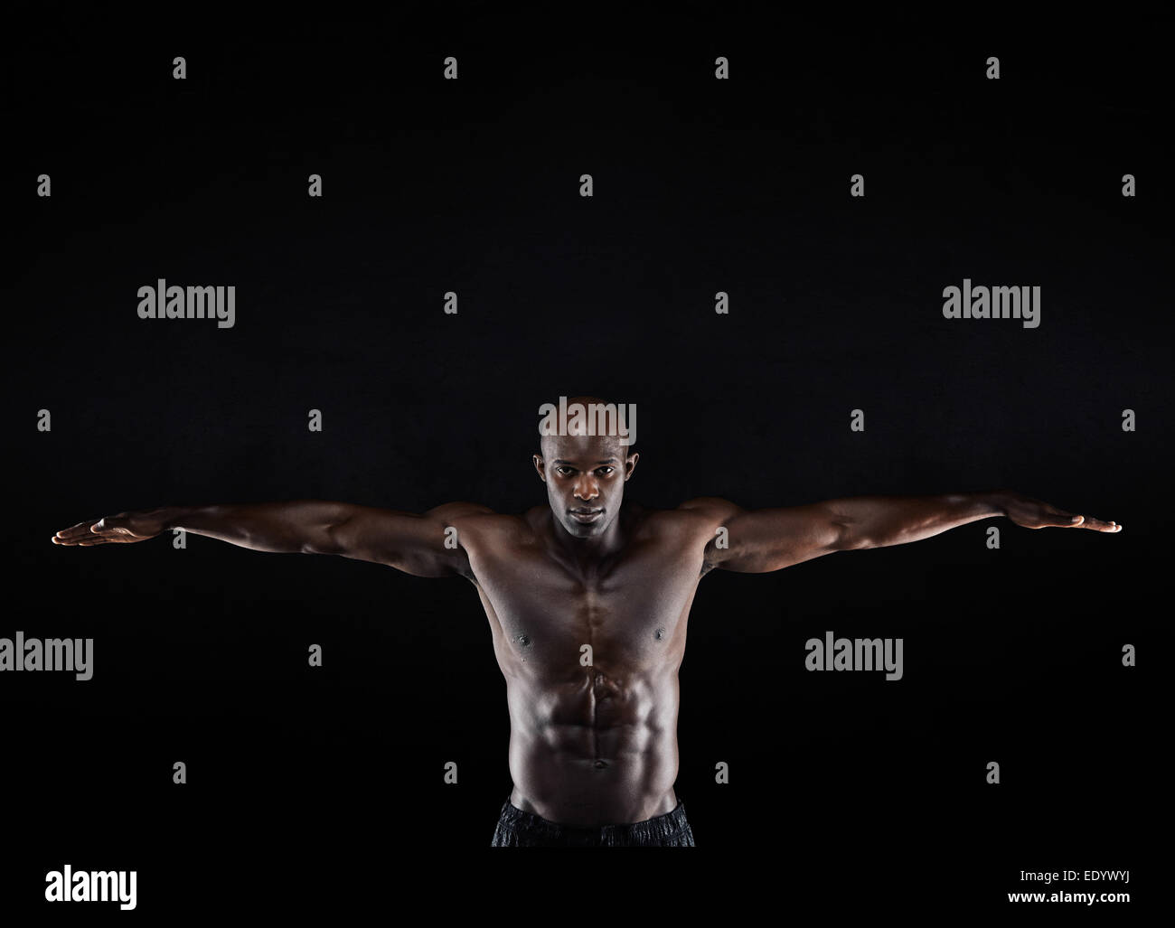 Ritratto di un forte giovane uomo muscolare stretching braccia contro uno sfondo scuro. Uomo di afro-americana in mostra il suo fisico. Foto Stock
