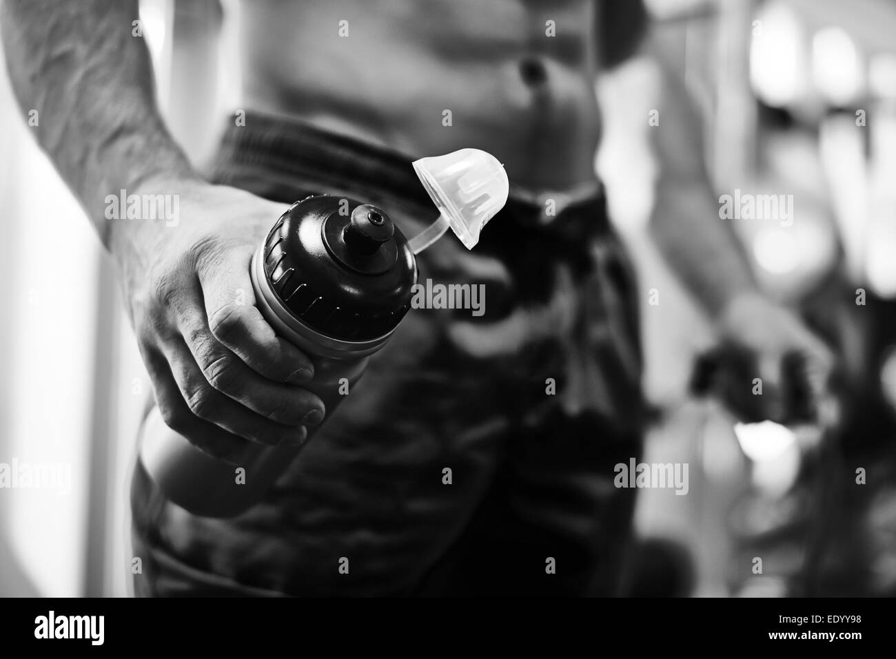 Mano di uno sportivo tenendo aperta la bottiglia di plastica con acqua in palestra Foto Stock
