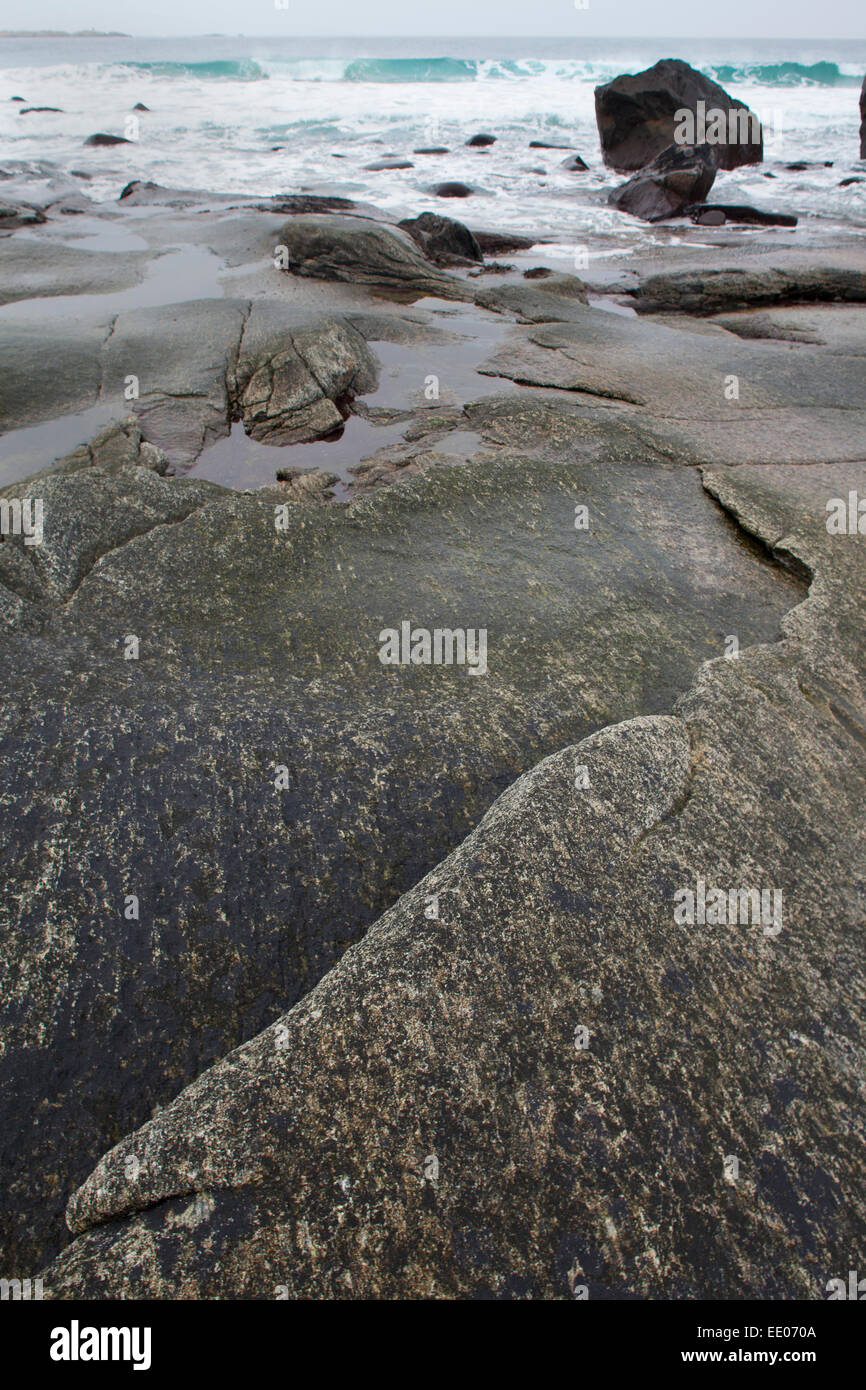 Scena costiere con lastre di roccia in primo piano e boulder e navigare in distanza, Utakleiv, Isole Lofoten, arctic Norvegia. Foto Stock