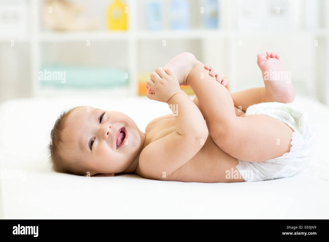 Il Bambino giacente sul letto bianco e tenendo le gambe Foto Stock
