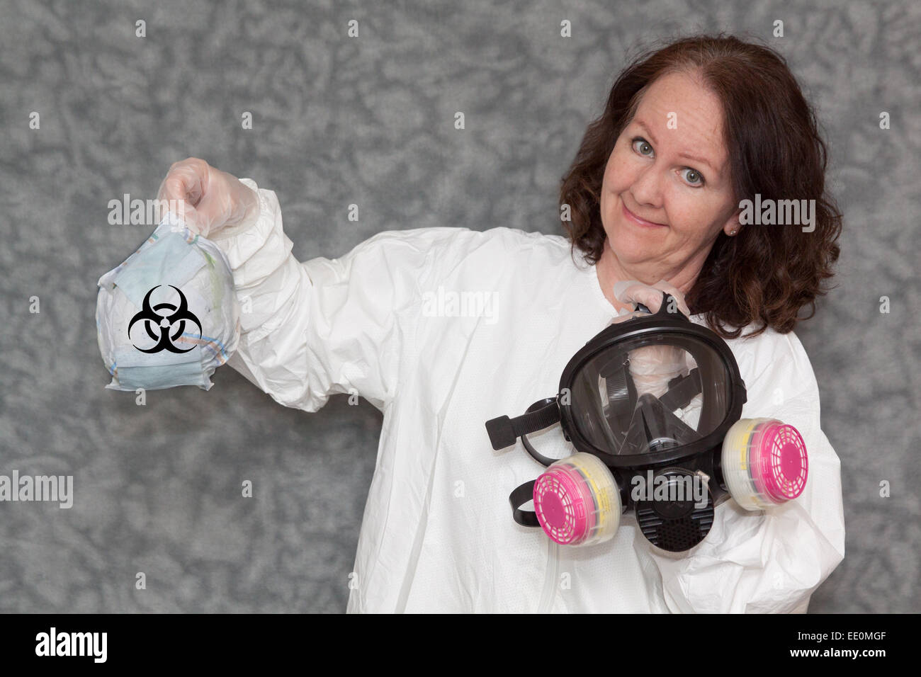 La donna è in possesso di una maschera a gas in una mano e cestino con il simbolo di rischio biologico nelle altre, con uno sfondo neutro Foto Stock