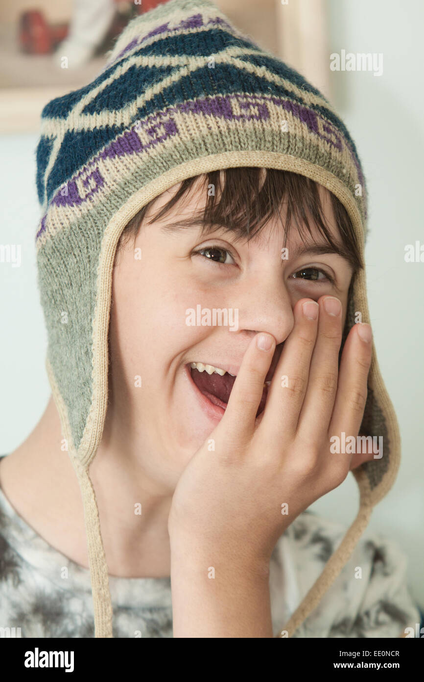 Attraente ragazzo adolescente con autismo e sindrome di Down è ridere come egli mette sul suo inverno cappello di lana Foto Stock