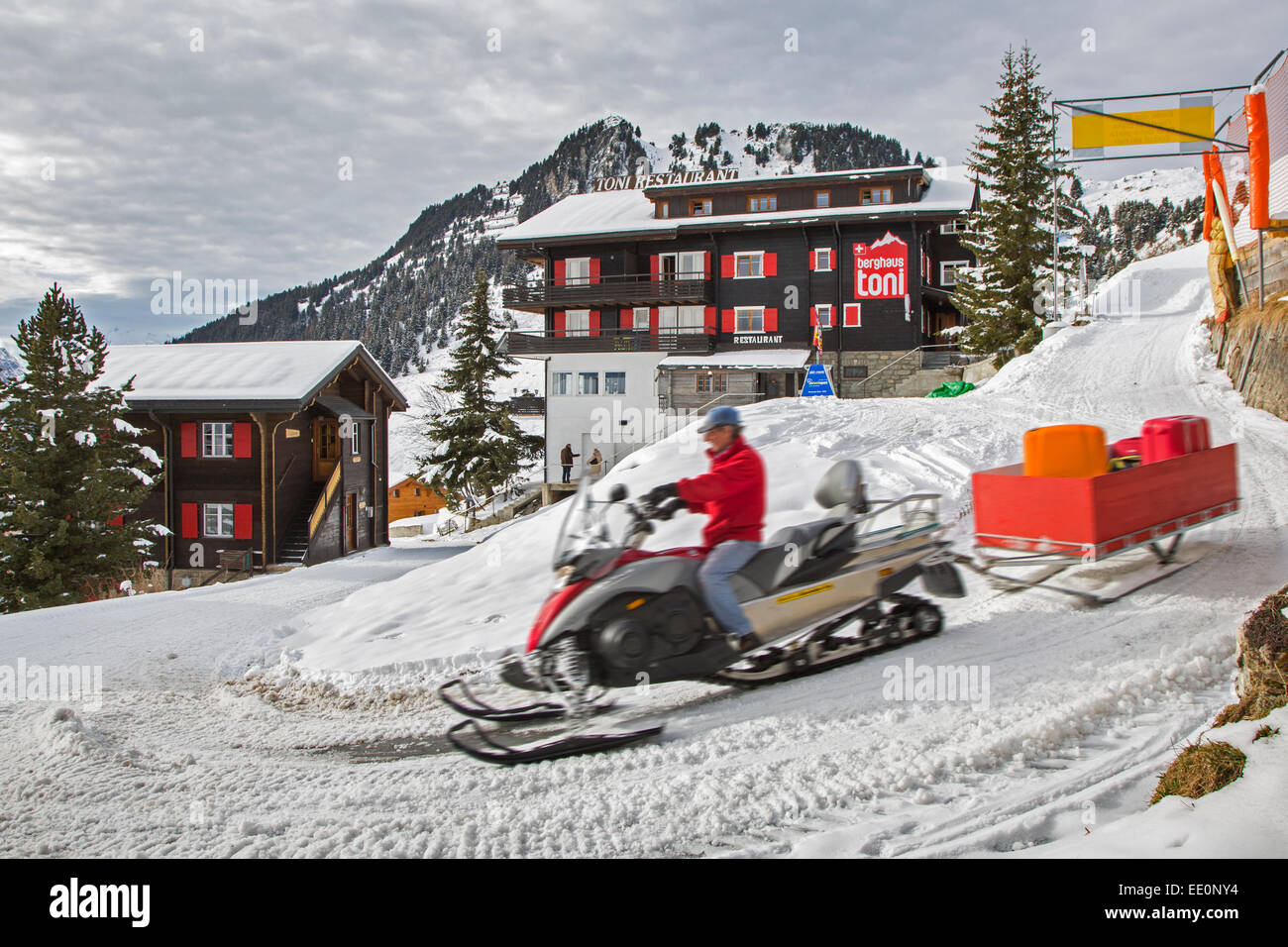 Uomo in motoslitta portando i bagagli da turisti in hotel nel villaggio Riederalp in inverno, Wallis / Valais, Svizzera Foto Stock