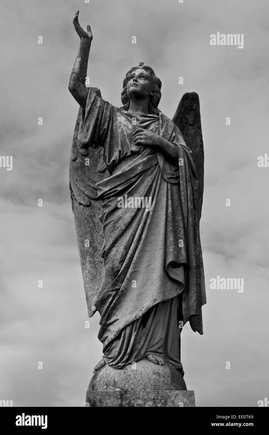 Angelo scolpito su un plinto di marmo con braccio esteso verso l'alto. Monocromatico Foto Stock