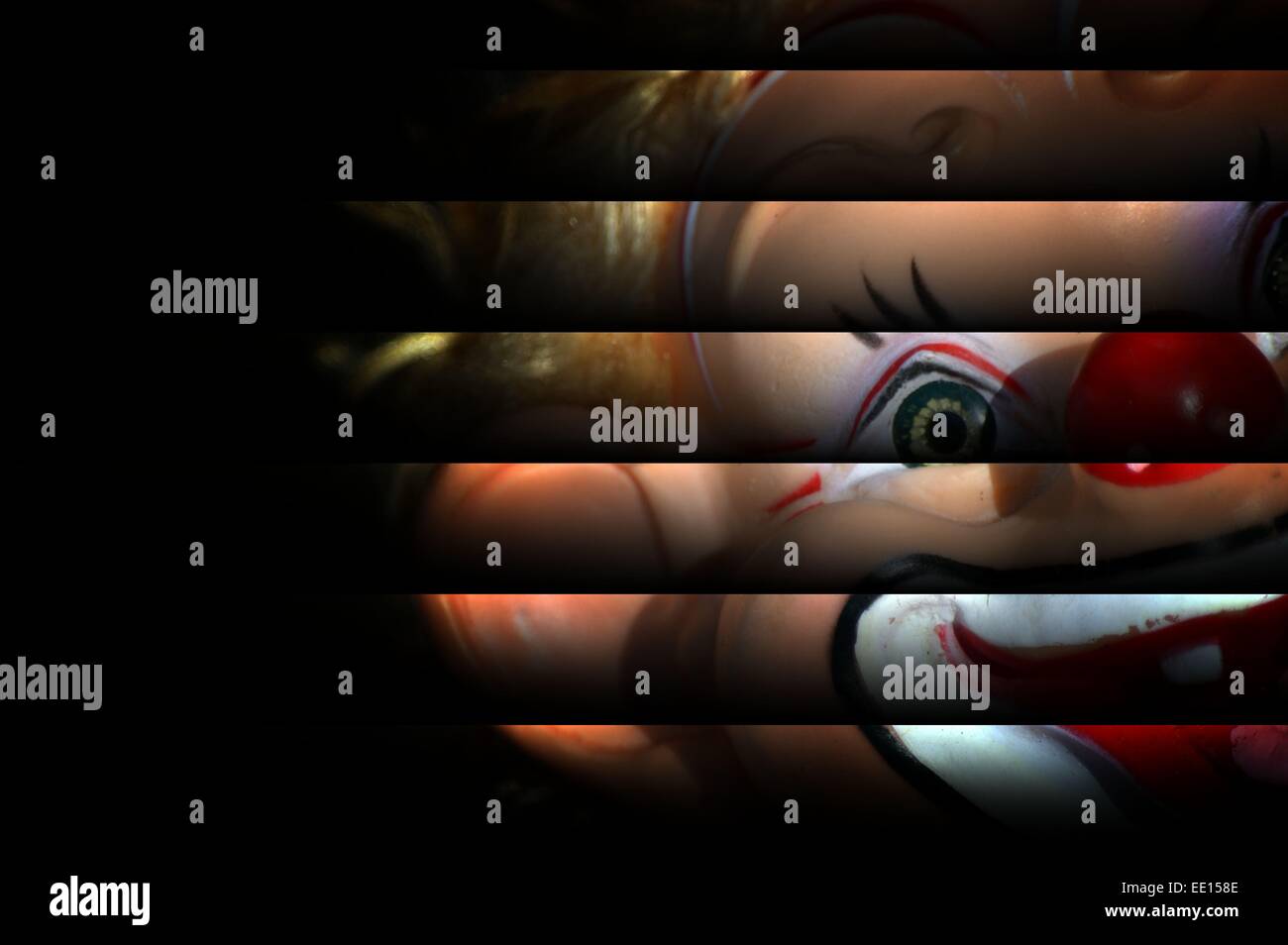 Scary clown doll appaiono essere il peering attraverso le persiane. clown su sfondo scuro,la metà della faccia di clown staring Foto Stock