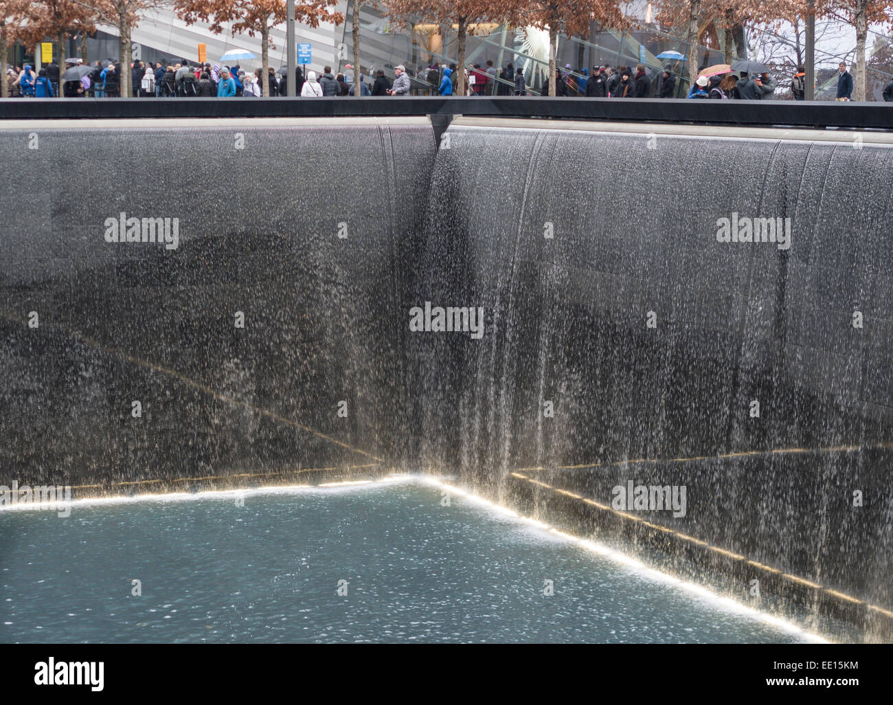 Caduta di acqua a settembre xi memorial a Ground Zero. I turisti, sfidando la pioggia con ombrelloni, circondano il pozzo profondo Foto Stock