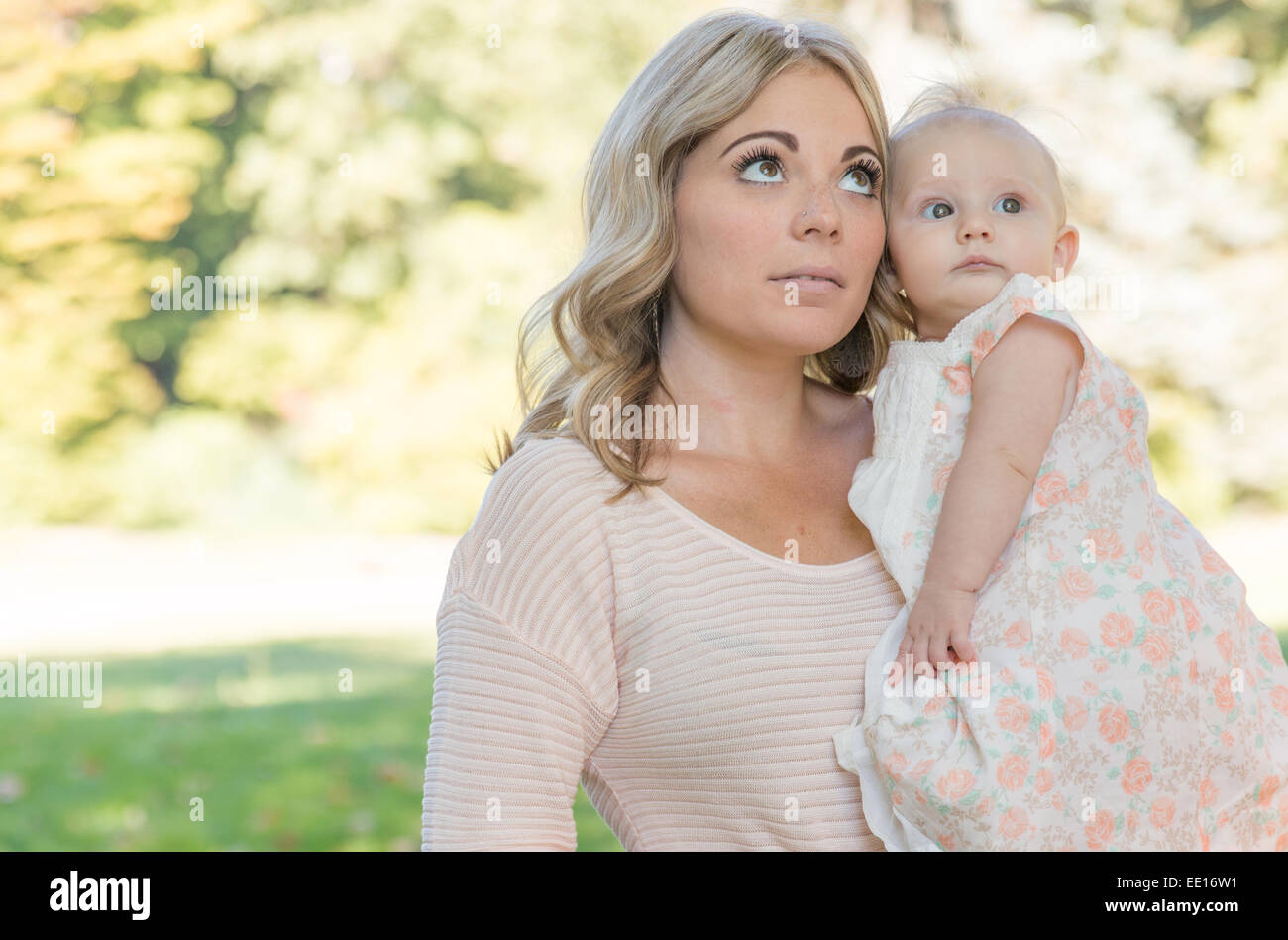 Bionda e giovane azienda madre sei mesi Baby girl cercando nel parco soleggiato Foto Stock