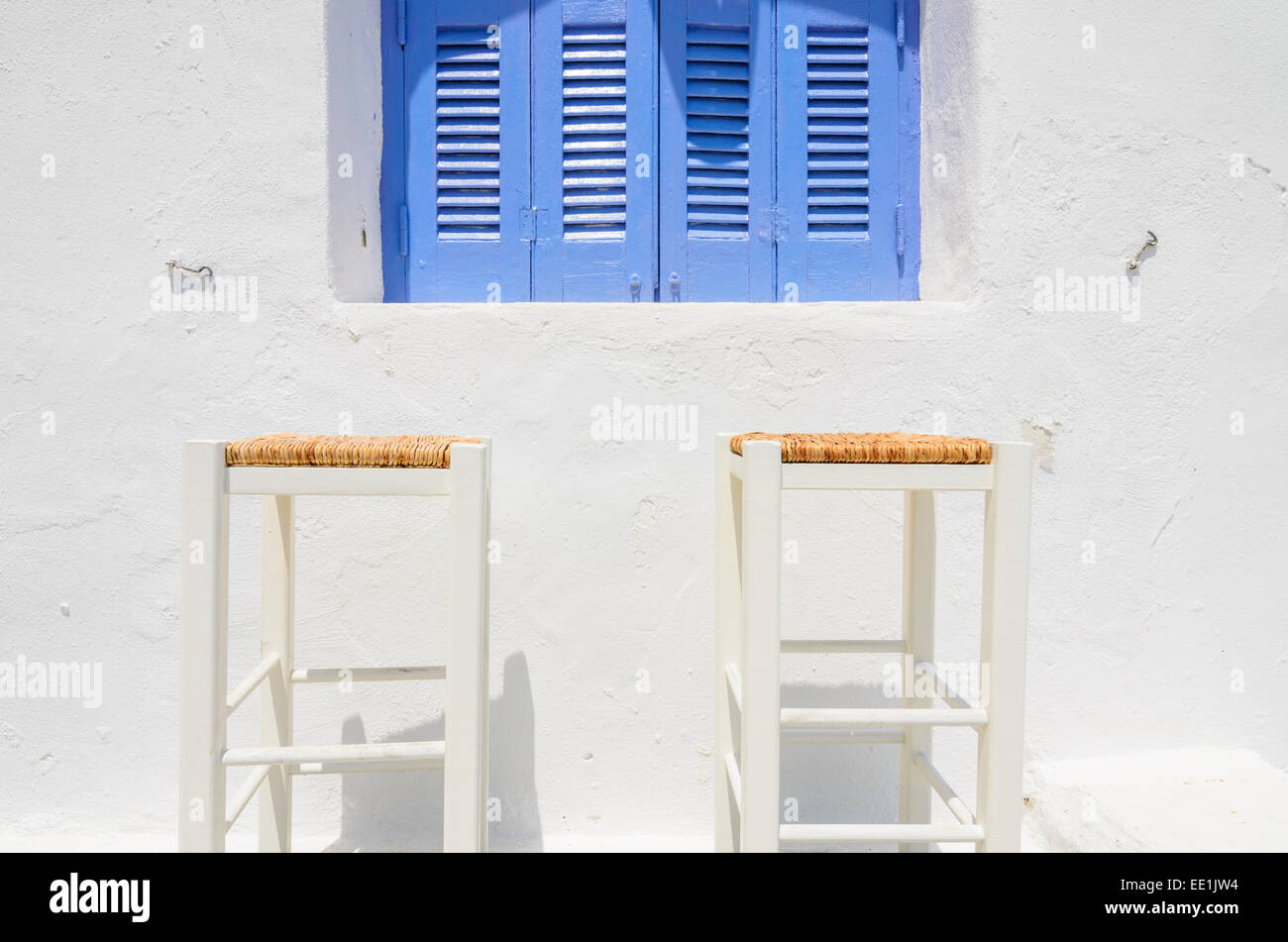 Due bianchi Sgabelli in legno contro un bianco-lavato parete sotto un blu nella finestra lucernario, Naoussa, Paros, Cicladi Grecia Foto Stock