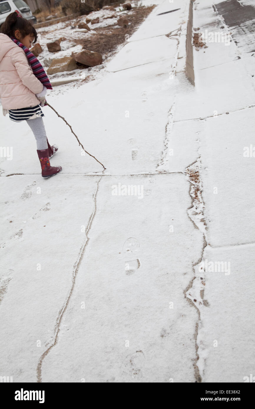 Bambina di cinque anni si trascina un bastone attraverso la neve fresca, la realizzazione di una linea verso il basso il suo marciapiede Foto Stock