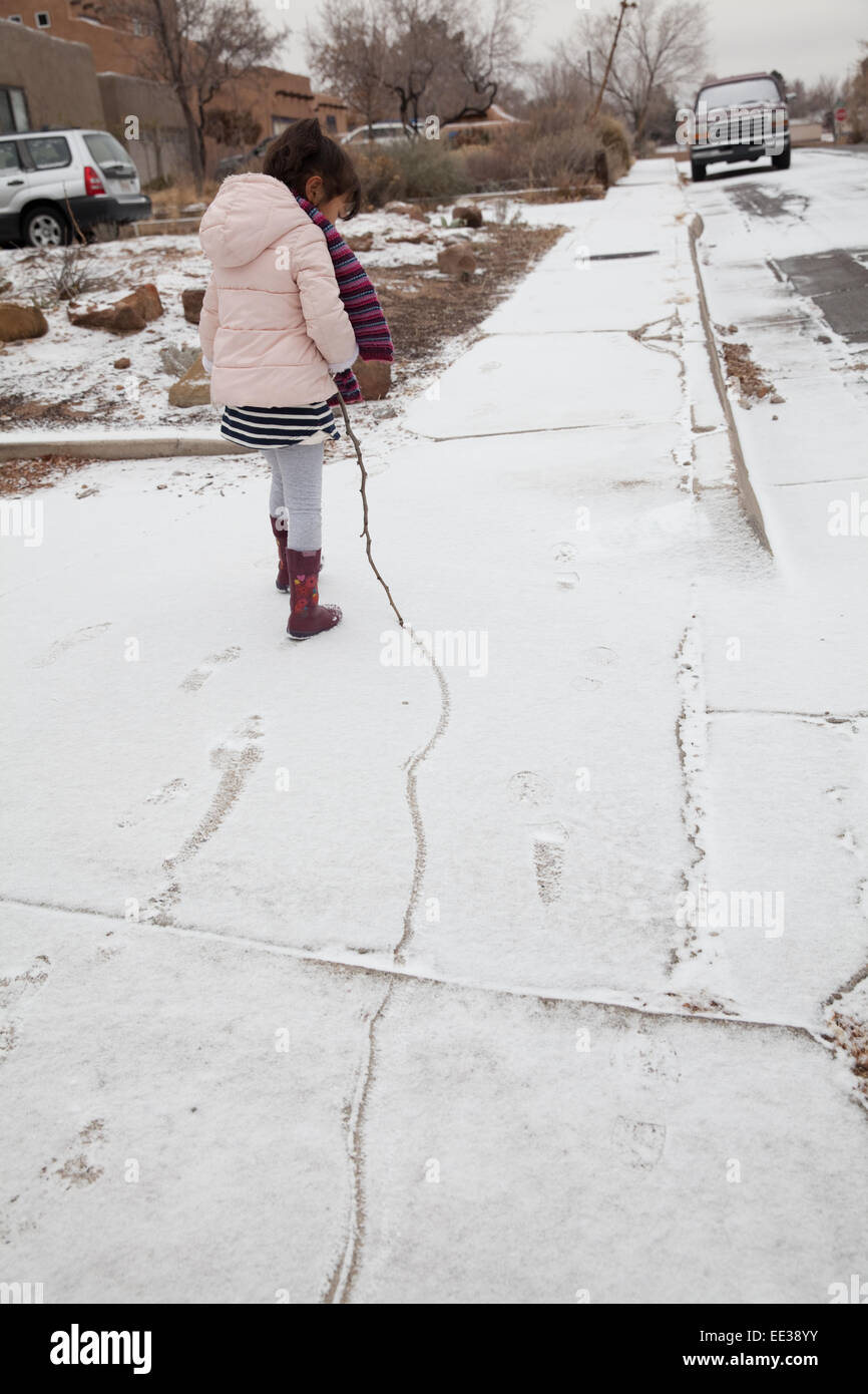 Bambina di cinque anni disegna una linea nella neve con un bastone. Foto Stock