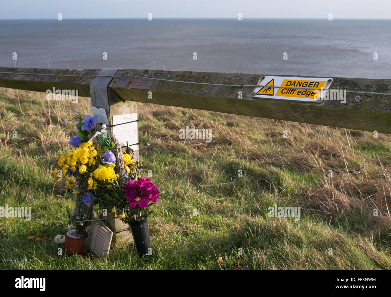 Pericolo Cliff segno bordo a fianco di un memoriale floreali a Seaham, North East England, Regno Unito Foto Stock