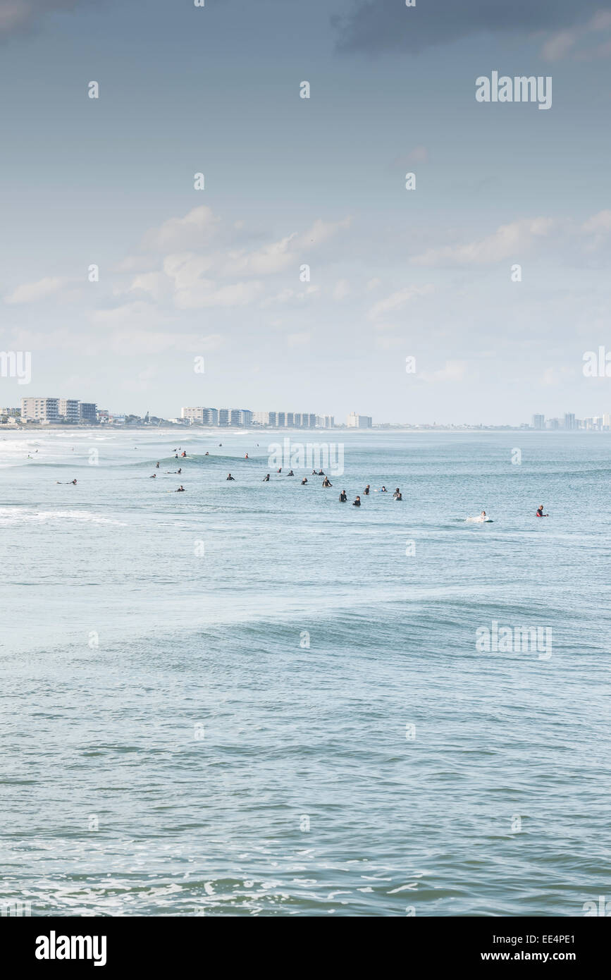 Molti surfisti in attesa di un'onda come un rigonfiamento rotoli da con il Daytona Beach, Florida skyline in background. Foto Stock