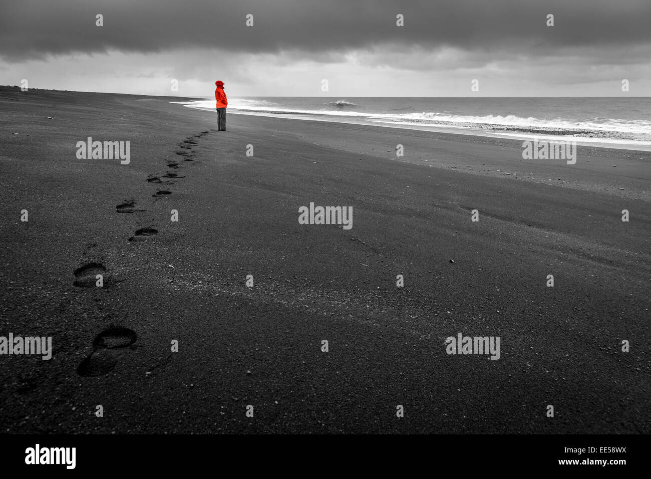 Una donna sta guardando le onde su una spiaggia di sabbia nera nel sud dell'Islanda Foto Stock