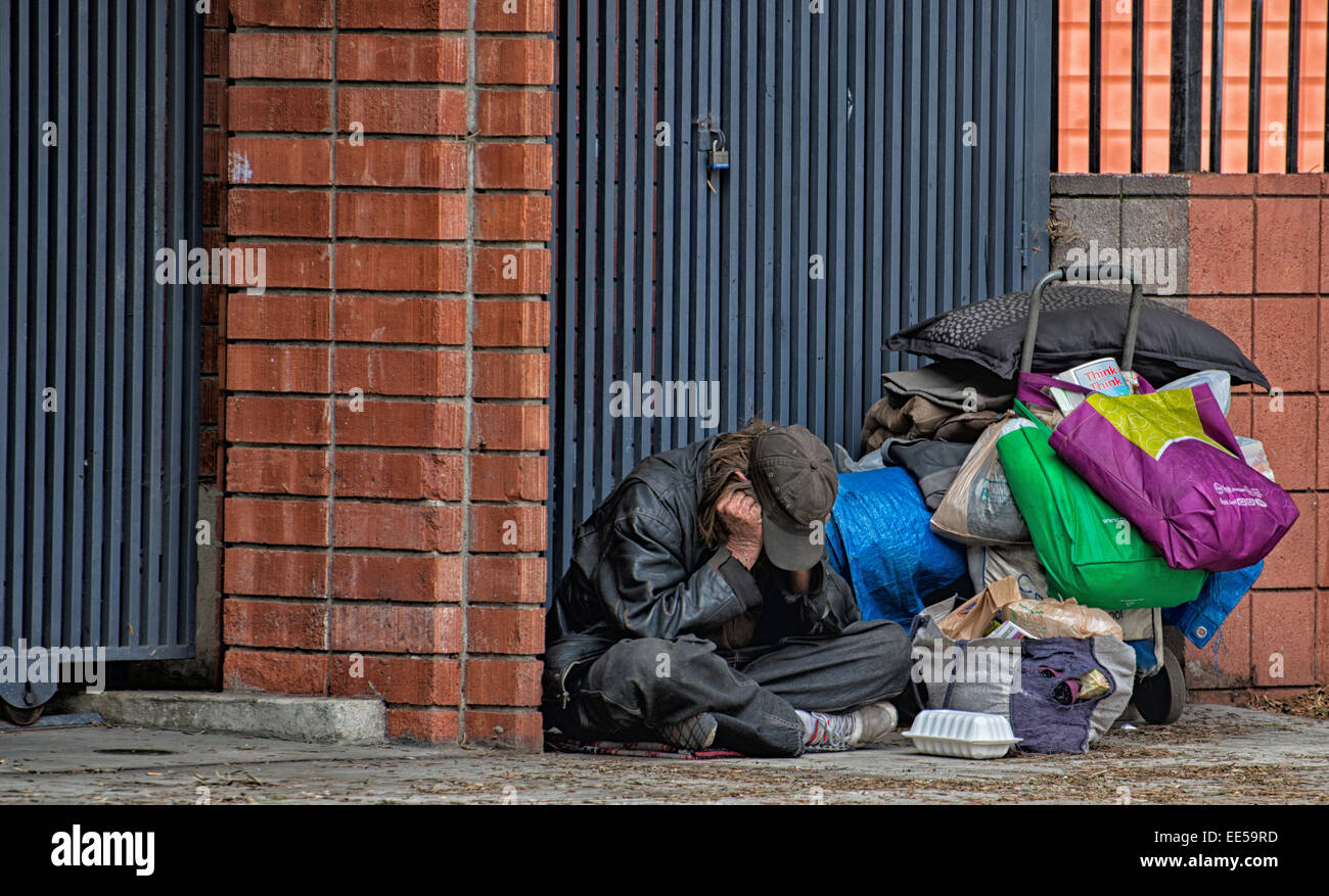 Senzatetto uomo seduto sul marciapiede accanto alla costruzione e al carrello, East Village, San Diego, California USA Foto Stock