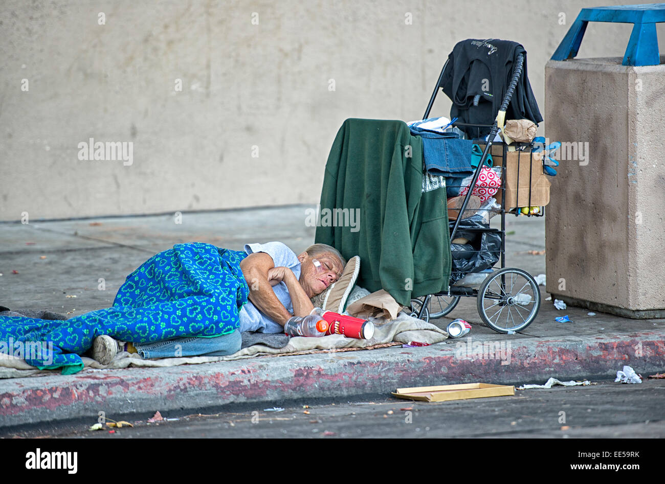 Senzatetto anziani donna che dorme sul marciapiede accanto al carrello della spesa e nel Cestino, East Village, San Diego, California USA Foto Stock