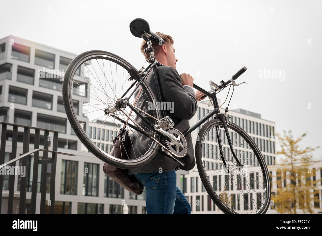 Giovane imprenditore che porta bicicletta, Monaco di Baviera, Germania Foto Stock