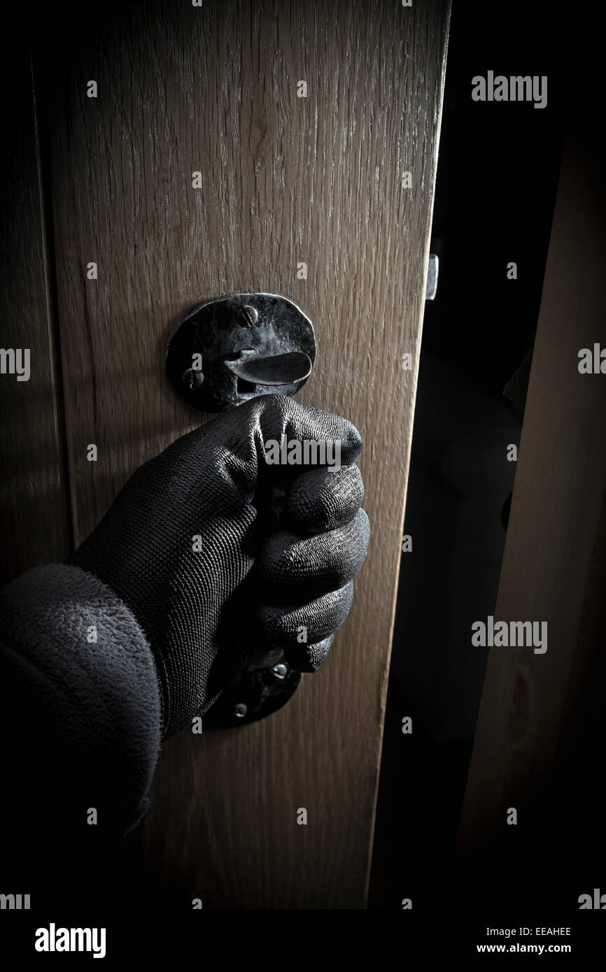 La mano guantata aprendo una porta in una stanza buia. Foto Stock