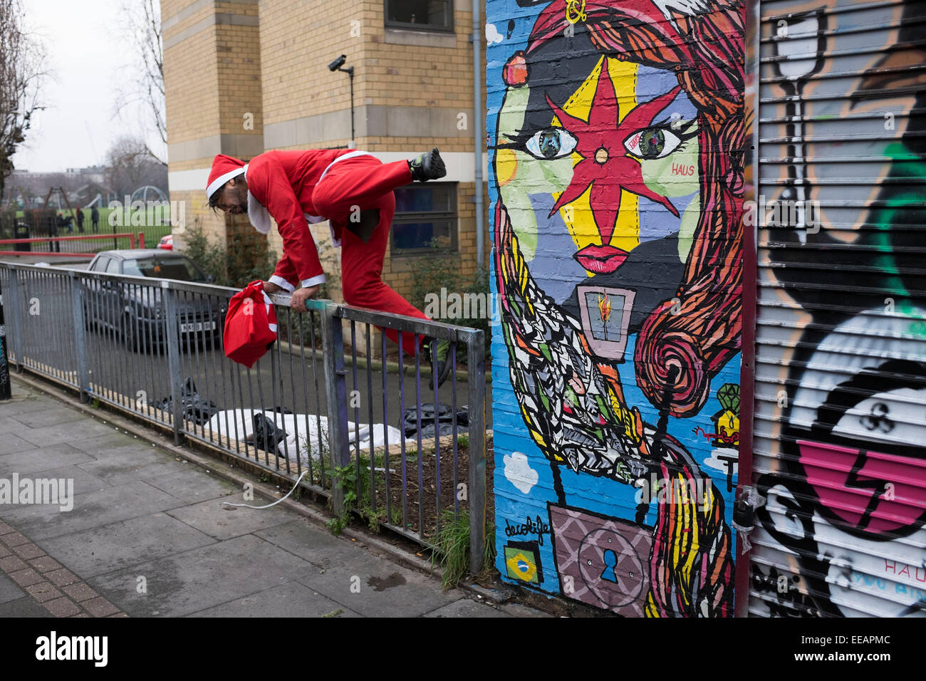 Uomo vestito da Santa Claus salta sopra un recinto vicino a Brick Lane, Londra, Regno Unito. Come Natale arriva a un vicino egli è visto correre lontano come se colpevole di un qualche tipo di reato. Foto Stock