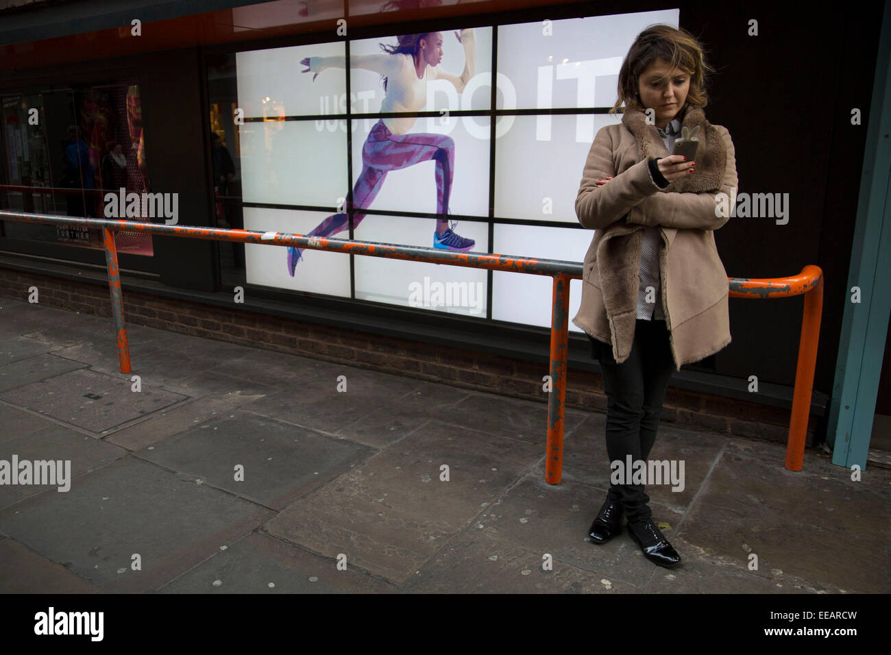 Pubblicità Nike runner corre lungo una barriera vicino gli ignari cittadini. Il video annuncio pubblicitario con lo slogan "Just Do It con una donna che attraversano lo schermo rende per un'illusione ottica di sorta ed una strana scena urbana. Londra, Regno Unito. Foto Stock