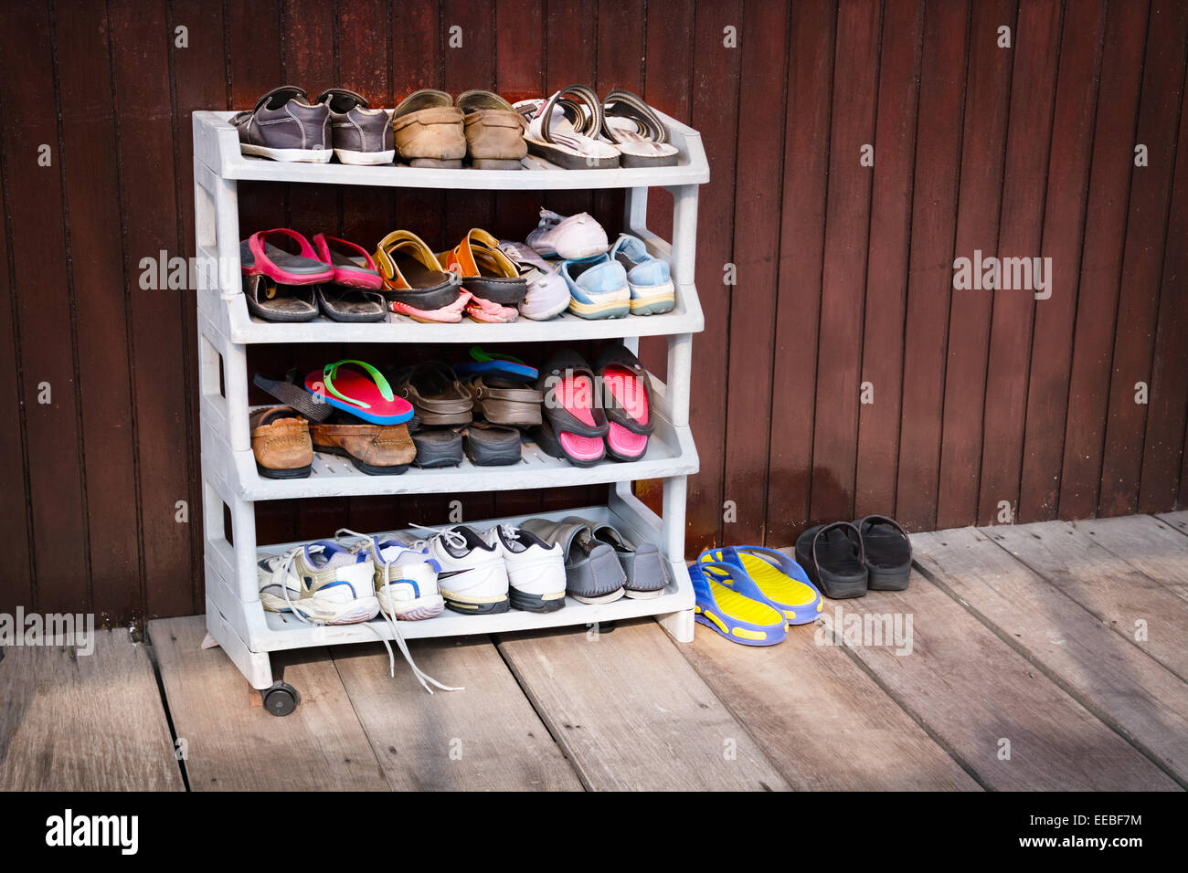 Una varietà di scarpe colorate, perfettamente ordinato su un pattino di plastica cremagliera al di fuori di una casa in legno. Foto Stock