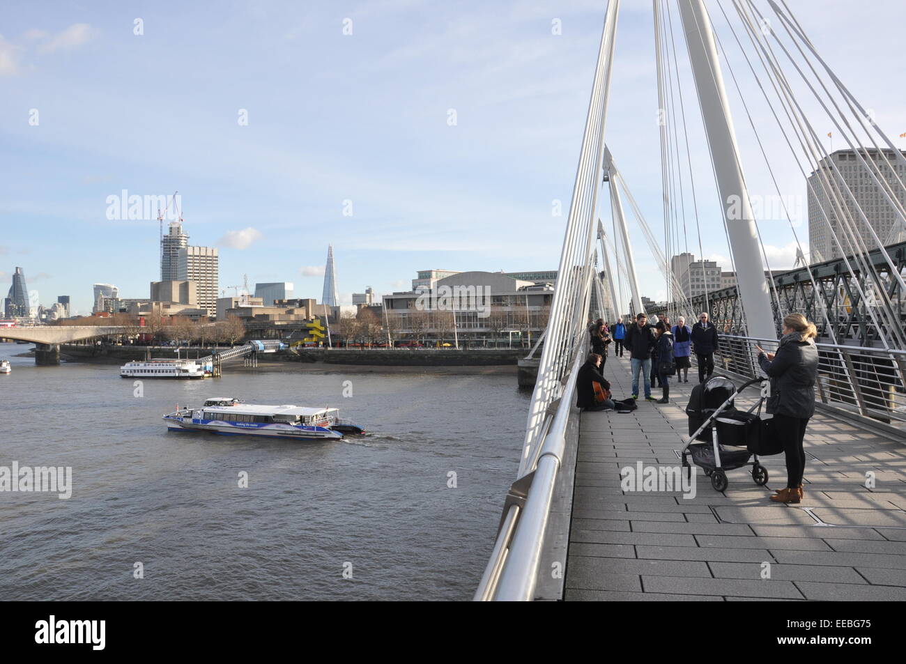 Le persone che attraversano il ponte a Hungerford attraverso il Tamigi a south bank, con imbarcazioni da fiume e Royal Festival Hall di Londra Foto Stock