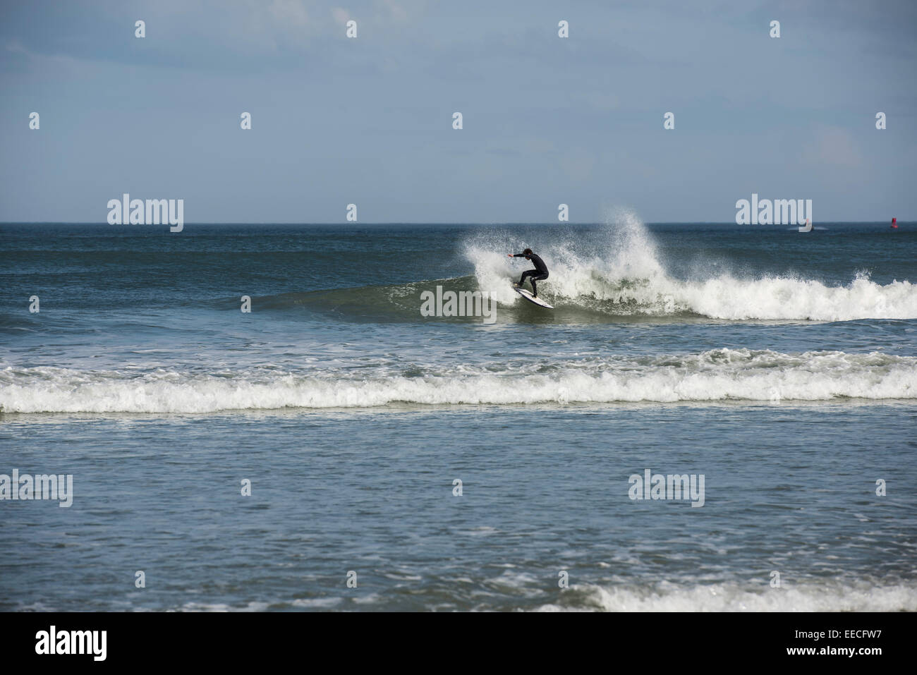 Una solitaria giovane uomo in nero di una muta umida è indietro di taglio su un'onda come egli surf litorale orientale della Florida vicino a Daytona Beach. Foto Stock