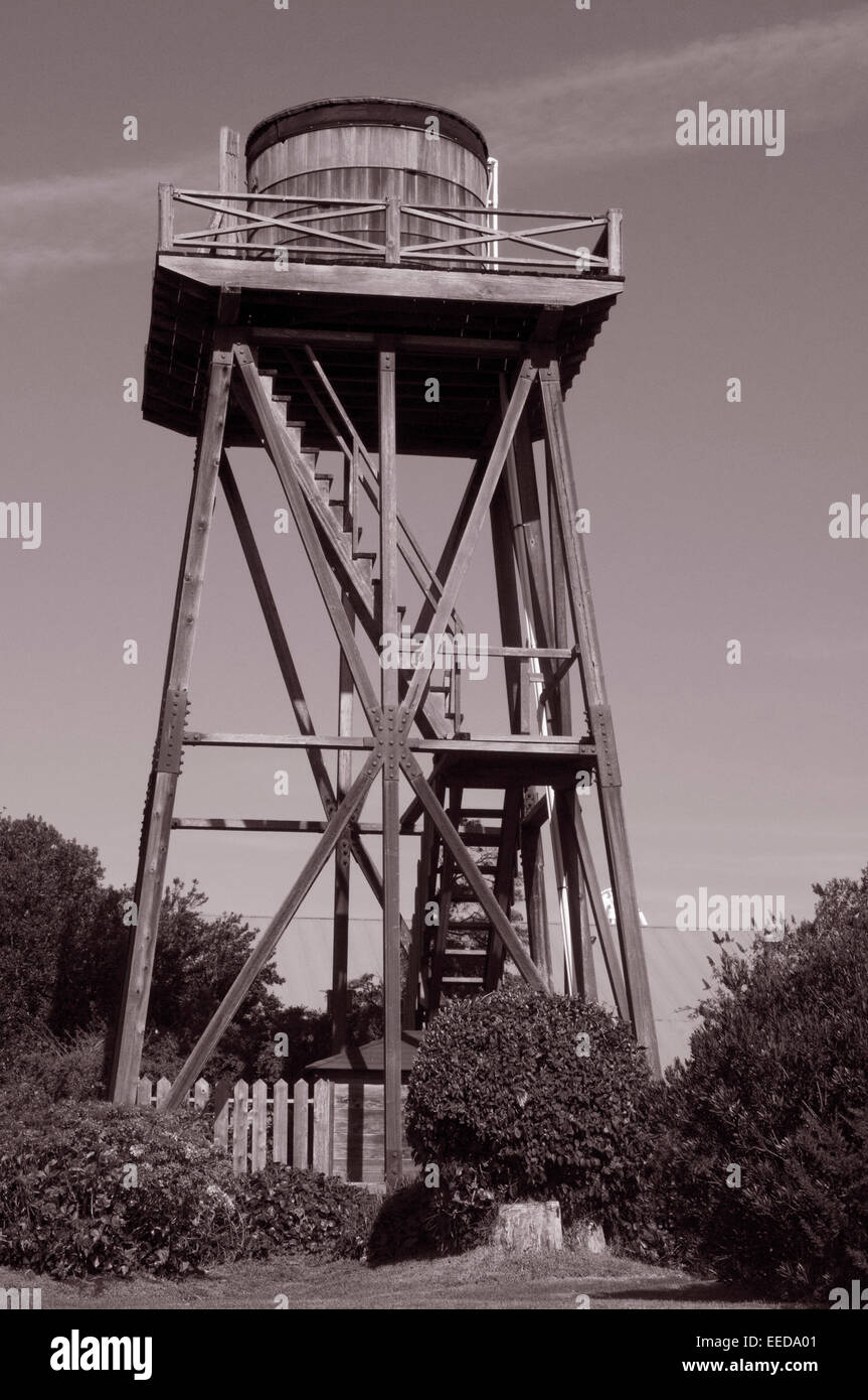 Mendocino in legno torre di acqua in colore seppia con circostante in legno rustico fattorie e arbusti Foto Stock
