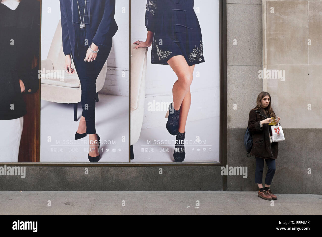 Ragazza il rotolamento e fumare una sigaretta in piedi accanto ad alcune grandi immagini pubblicitarie al di fuori di un negozio di moda. Londra, Regno Unito. Foto Stock