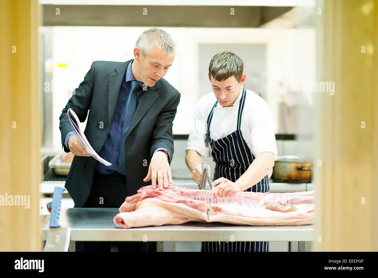 Un manager di insegnamento di una partecipante macellaio come tagliare la carne Foto Stock