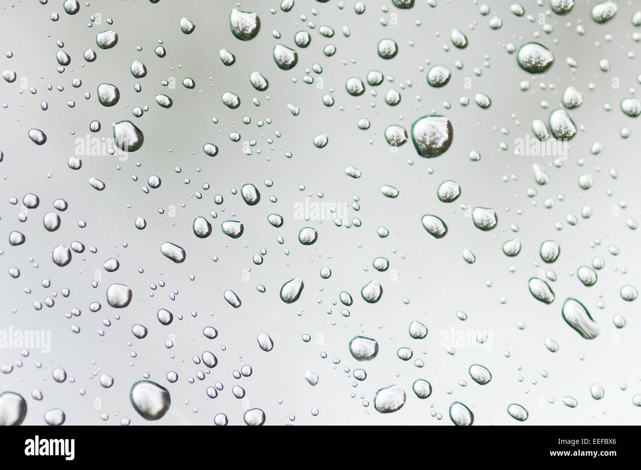 Le goccioline di acqua sul vetro chiari riflettono la luce ambiente produrre interessanti modelli. Foto Stock