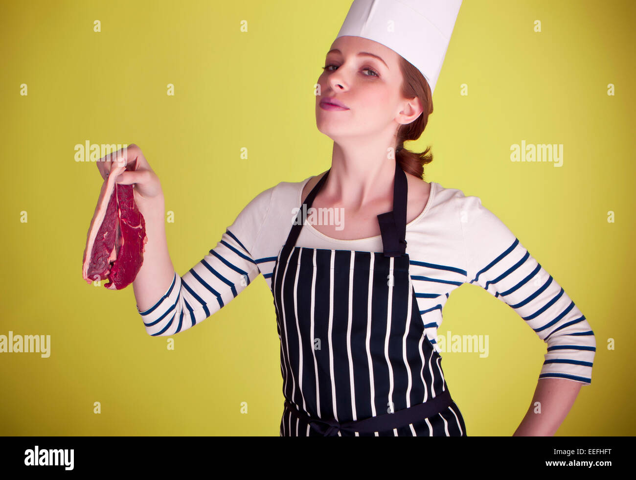Un giovane e attraente chef femmina tenendo un bel pezzo di bistecca pronti per essere cucinati alla perfezione. Foto Stock
